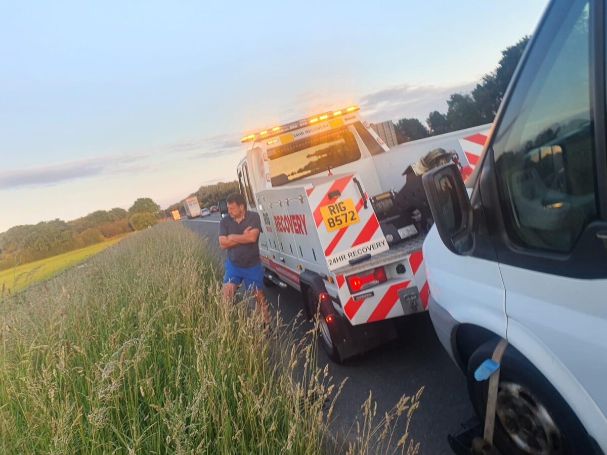 Breakdown Man's RIG 8572 24-hour recovery truck on a grass verge next to a white Transit van on a summer evening callout.