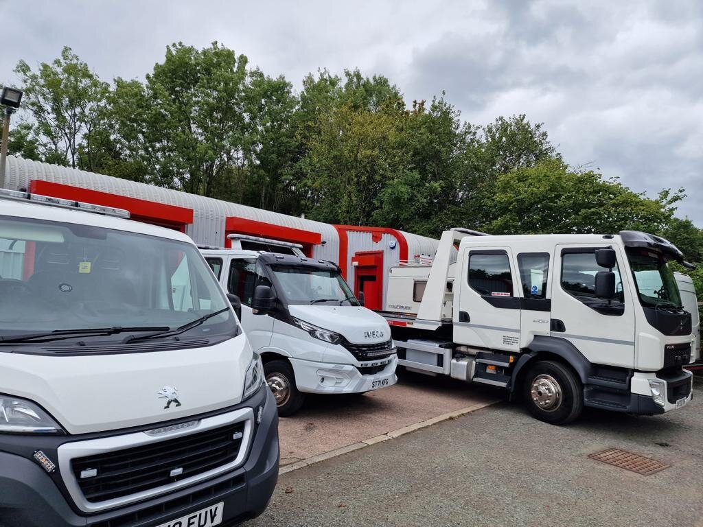 A Peugeot Boxer van, Iveco Daily van and DAF recovery truck parked side by side outside the Breakdown Man depot under cloudy skies.