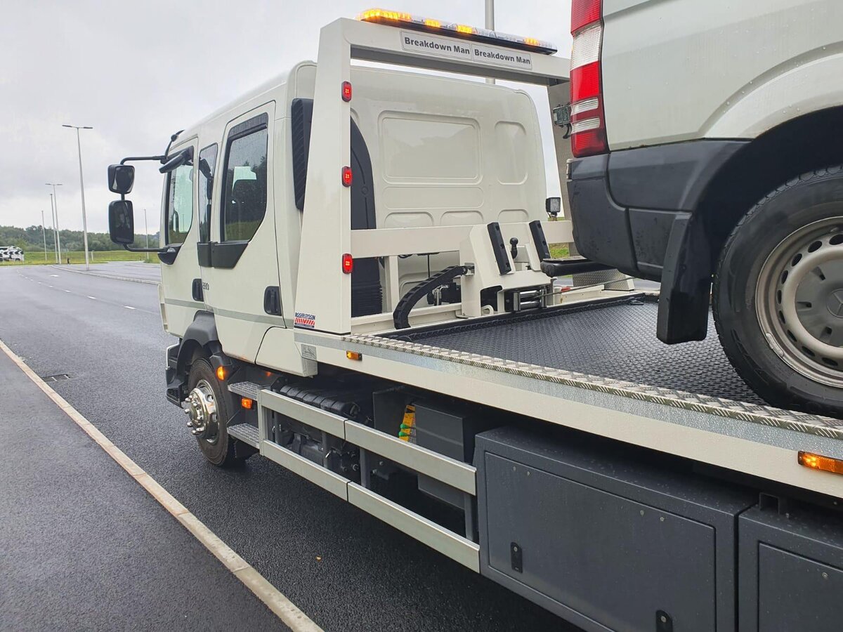 Breakdown Man branded recovery truck with a white panel van loaded up beside a slip road.