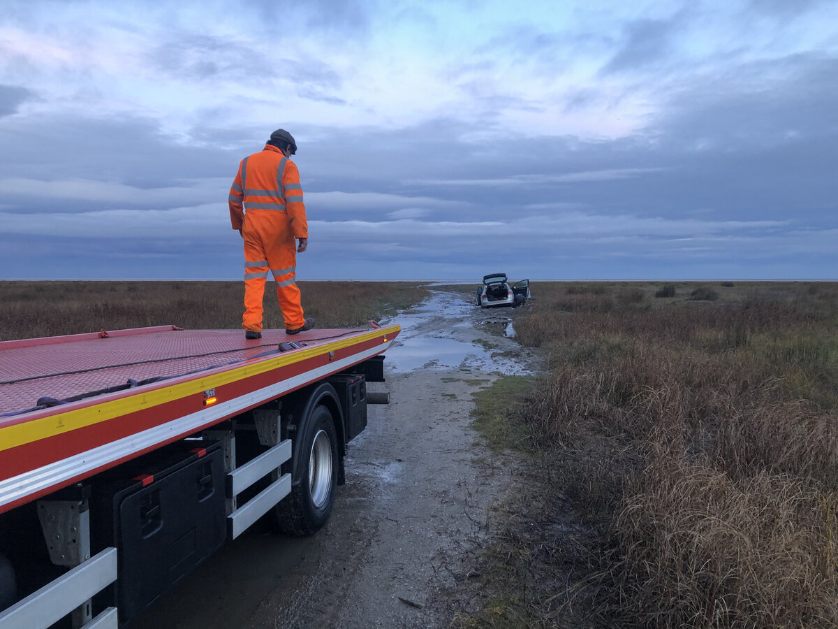Breakdown Man recovery operator preparing the recovery truck at dawn beside a vehicle stranded on a remote marshland track.