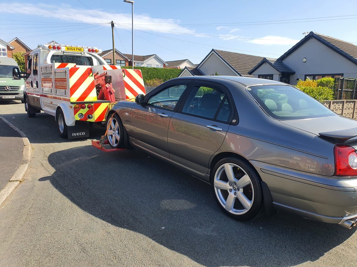 Breakdown Man recovery truck NX64 PNE loading a grey Rover 75 saloon on a sunny suburban street